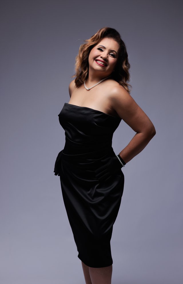 Mujer con vestido negro sin tirantes sobre un fondo claro de estudio.