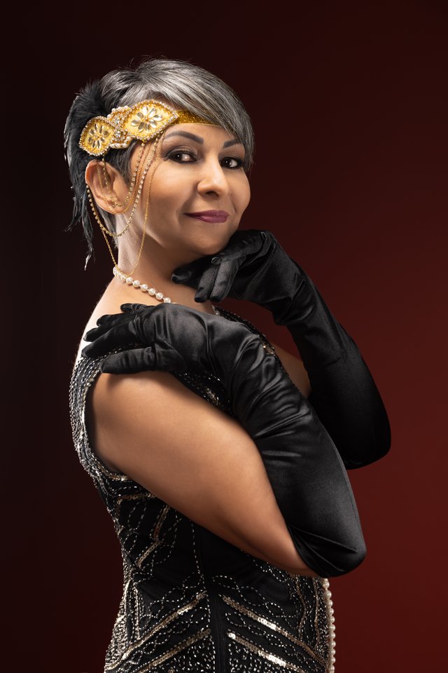 Mujer con turbante dorado, vestido de lentejuelas y guantes largos negros.