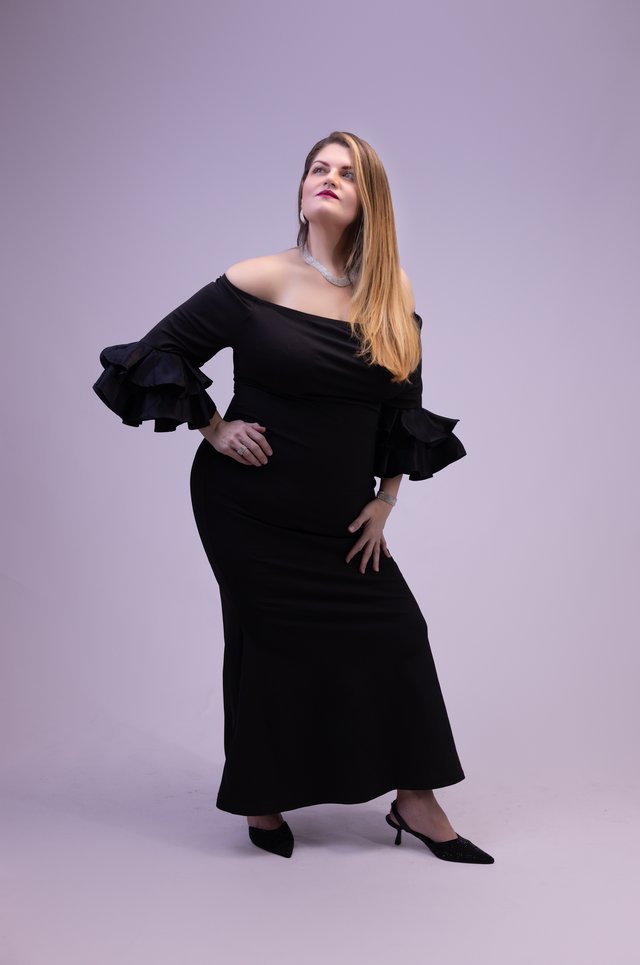Mujer con vestido negro de hombros descubiertos sobre un fondo claro.