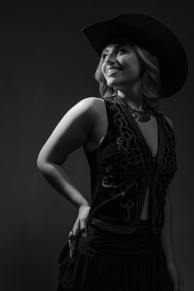 Retrato en blanco y negro de una mujer con sombrero y vestido bordado.