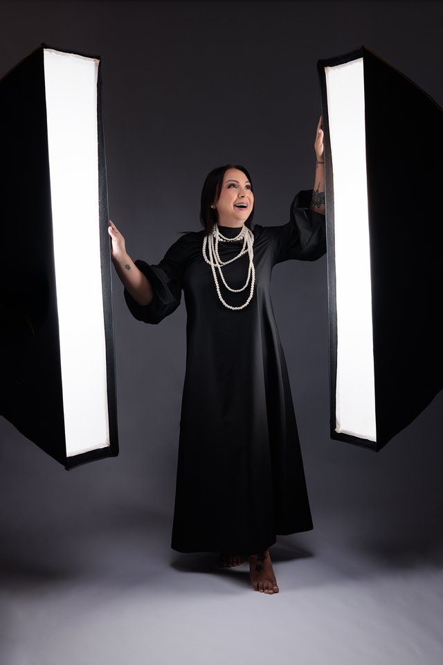 Mujer con vestido negro largo de pie entre dos paneles de luz.