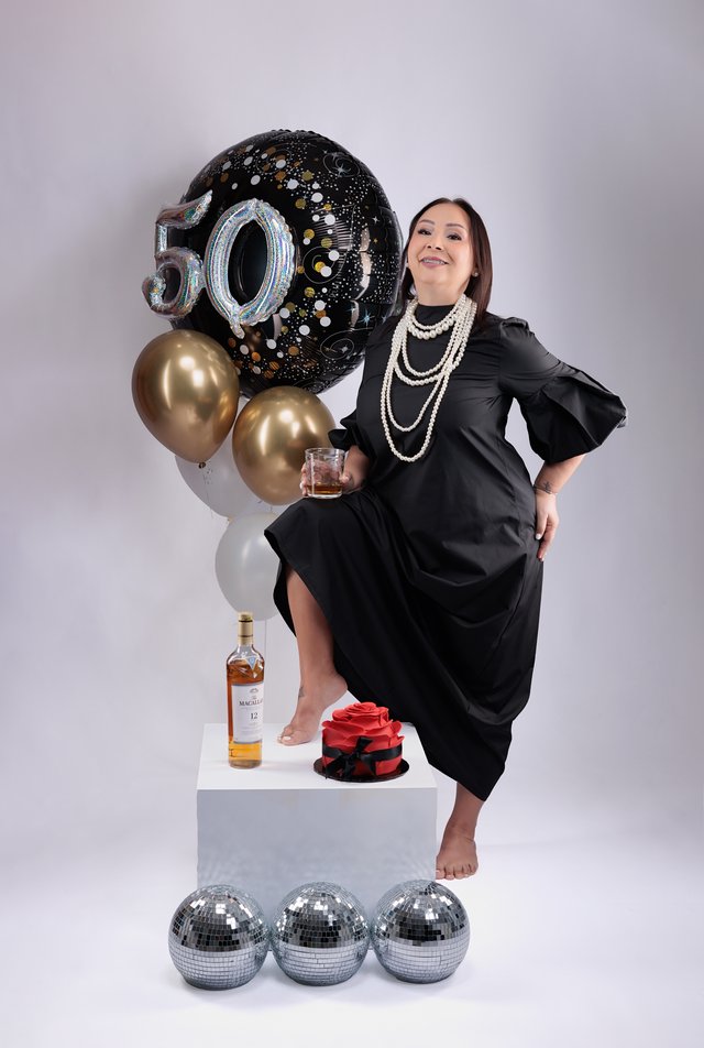 Mujer celebrando sus cincuenta años junto a globos negros y dorados.