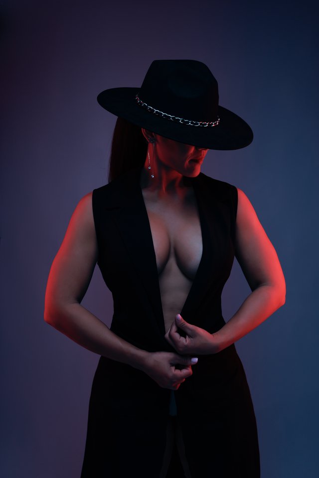 Mujer con sombrero negro iluminada con luz roja de contorno.