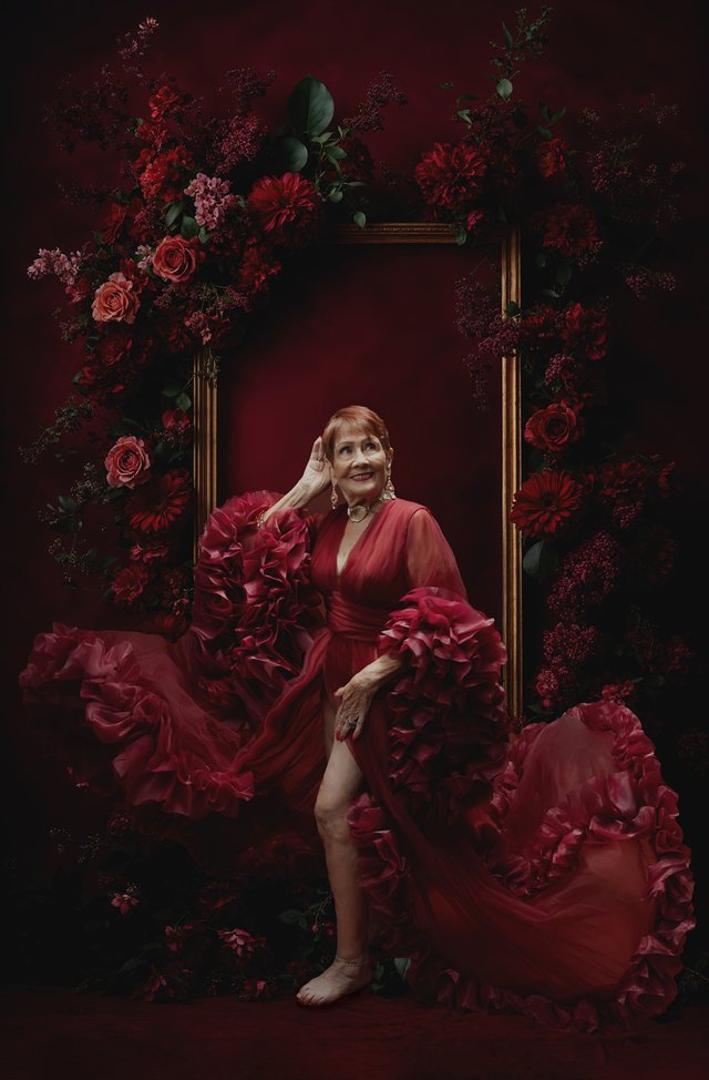 Mujer con vestido rojo sentada dentro de un marco de rosas rojas.